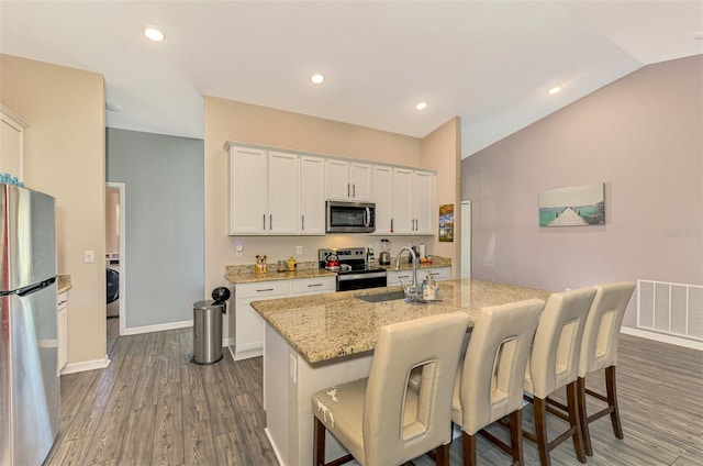 kitchen with a kitchen breakfast bar, light stone counters, stainless steel appliances, white cabinets, and an island with sink