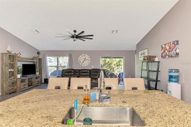 kitchen with ceiling fan, light stone counters, lofted ceiling, and sink