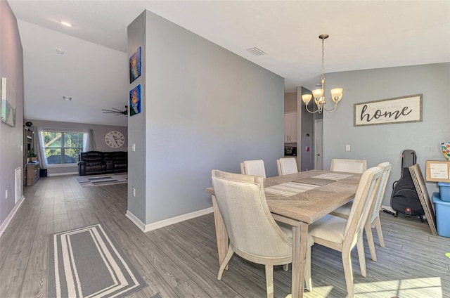 dining area with hardwood / wood-style floors, ceiling fan with notable chandelier, and vaulted ceiling