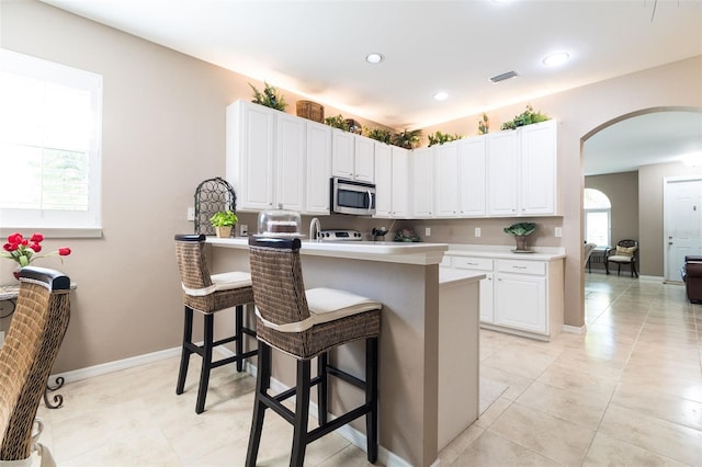 kitchen featuring a breakfast bar area, kitchen peninsula, white cabinetry, and light tile patterned flooring