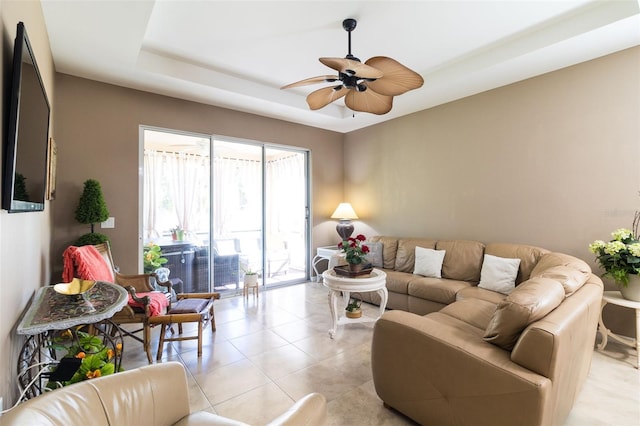 tiled living room with ceiling fan and a tray ceiling