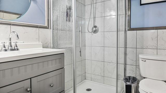 bathroom with walk in shower, vanity, toilet, and tile walls