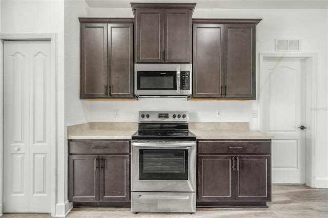 kitchen featuring dark brown cabinetry, light hardwood / wood-style flooring, and appliances with stainless steel finishes