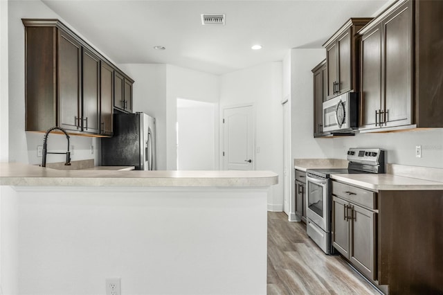 kitchen featuring kitchen peninsula, dark brown cabinetry, light wood-type flooring, and stainless steel appliances