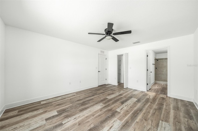 unfurnished bedroom featuring a walk in closet, ensuite bath, ceiling fan, hardwood / wood-style flooring, and a closet