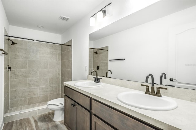 bathroom featuring hardwood / wood-style flooring, vanity, toilet, and tiled shower