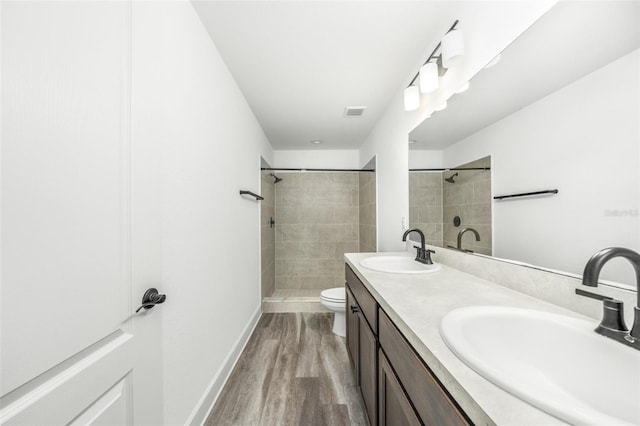 bathroom with tiled shower, vanity, wood-type flooring, and toilet