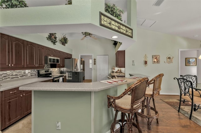 kitchen with lofted ceiling, ceiling fan, light wood-type flooring, tasteful backsplash, and stainless steel appliances