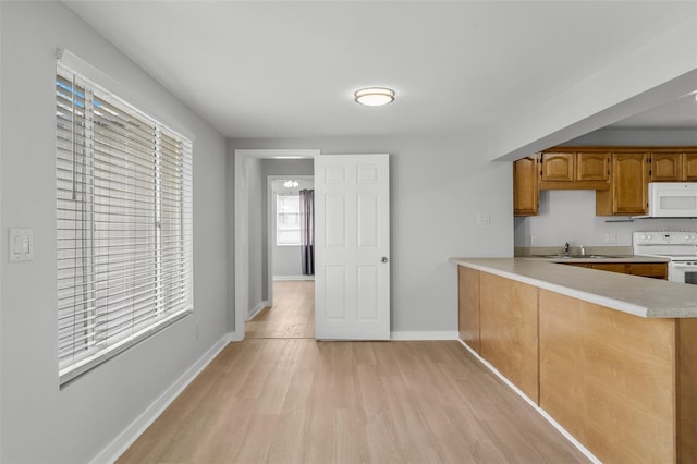 kitchen with kitchen peninsula, sink, light hardwood / wood-style floors, and white appliances