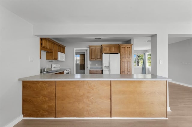 kitchen featuring kitchen peninsula, sink, light hardwood / wood-style floors, and white appliances