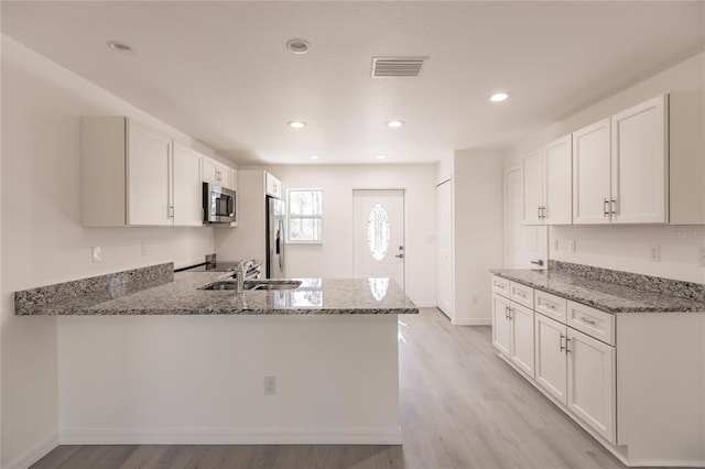 kitchen with white cabinets, light stone counters, kitchen peninsula, and stainless steel appliances