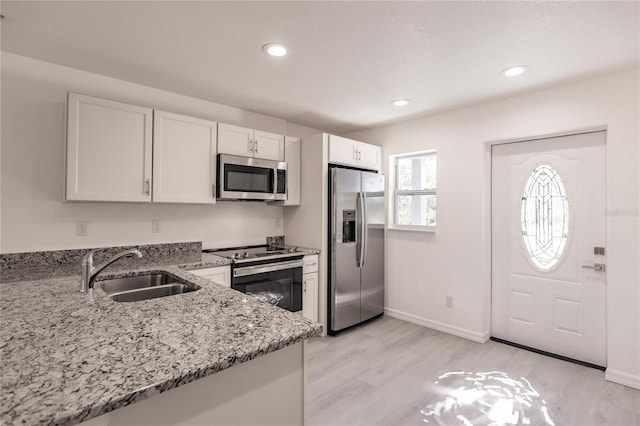 kitchen with sink, light wood-type flooring, appliances with stainless steel finishes, light stone counters, and white cabinetry