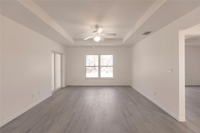 empty room featuring a raised ceiling, light hardwood / wood-style flooring, and ceiling fan