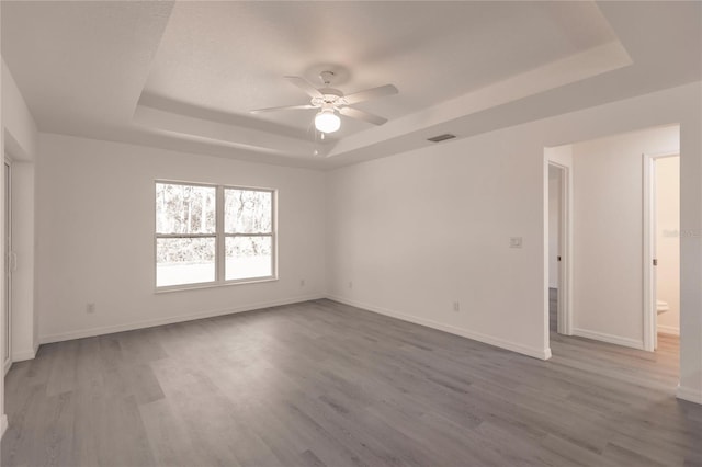 spare room with ceiling fan, wood-type flooring, and a tray ceiling