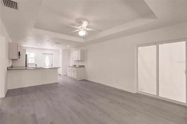 unfurnished living room featuring a tray ceiling, ceiling fan, sink, and light wood-type flooring