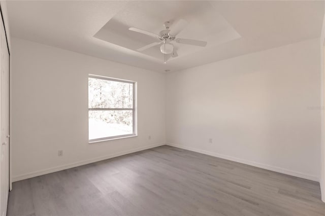 empty room featuring a tray ceiling, ceiling fan, and light wood-type flooring