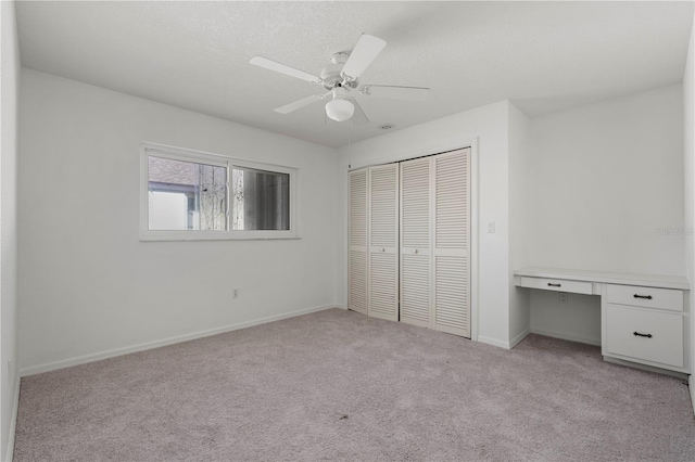 unfurnished bedroom featuring ceiling fan, built in desk, light carpet, and a closet