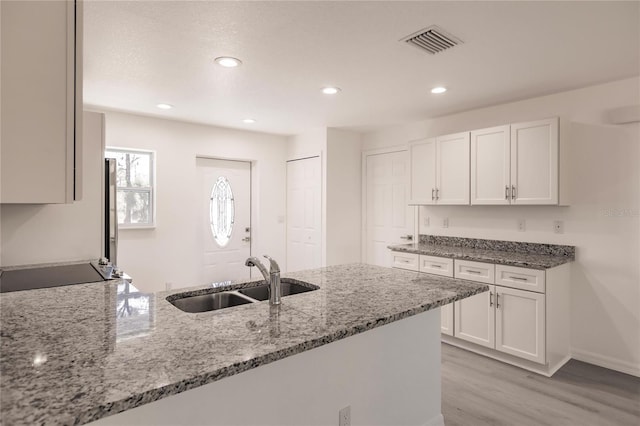 kitchen featuring white cabinets, black range oven, sink, light hardwood / wood-style floors, and light stone counters