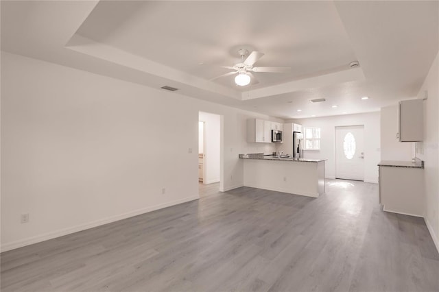 unfurnished living room featuring a tray ceiling, ceiling fan, and light wood-type flooring