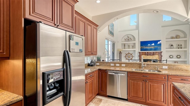 kitchen featuring appliances with stainless steel finishes, light stone counters, built in shelves, and sink