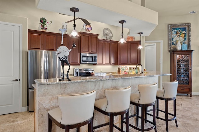 kitchen featuring a kitchen bar, appliances with stainless steel finishes, a center island with sink, and decorative light fixtures