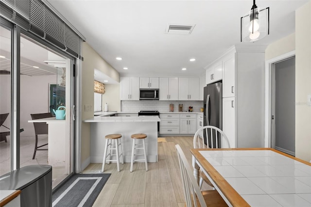 kitchen with hanging light fixtures, backsplash, a kitchen bar, white cabinets, and appliances with stainless steel finishes