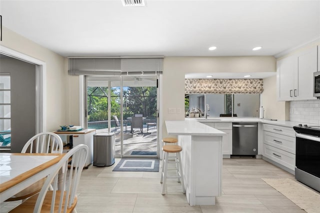 kitchen with white cabinets, decorative backsplash, kitchen peninsula, and appliances with stainless steel finishes