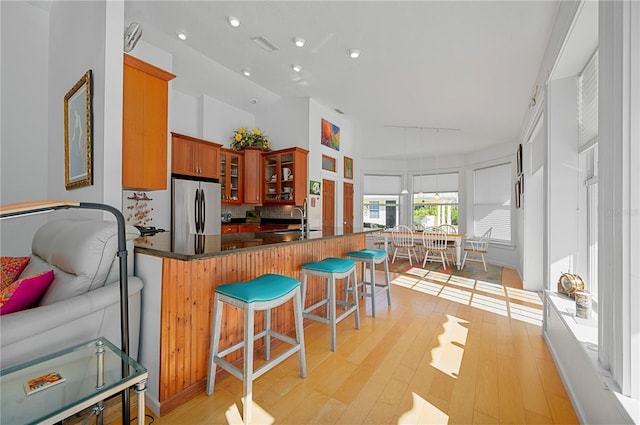 kitchen featuring kitchen peninsula, decorative backsplash, sink, light hardwood / wood-style flooring, and stainless steel refrigerator