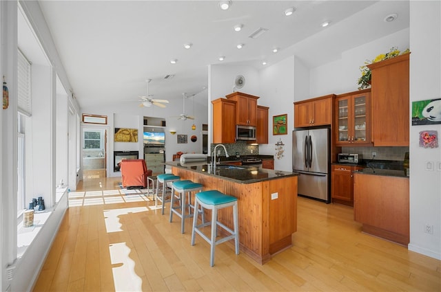 kitchen with appliances with stainless steel finishes, light wood-type flooring, tasteful backsplash, and high vaulted ceiling