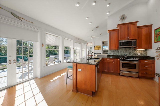 kitchen with ceiling fan, a center island, stainless steel appliances, high vaulted ceiling, and light hardwood / wood-style floors