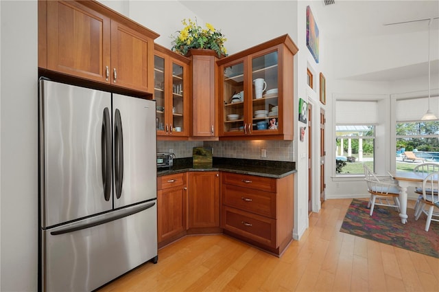 kitchen with decorative backsplash, stainless steel fridge, dark stone counters, high vaulted ceiling, and light hardwood / wood-style flooring