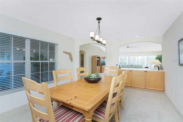 dining space with a textured ceiling, light colored carpet, and ceiling fan with notable chandelier