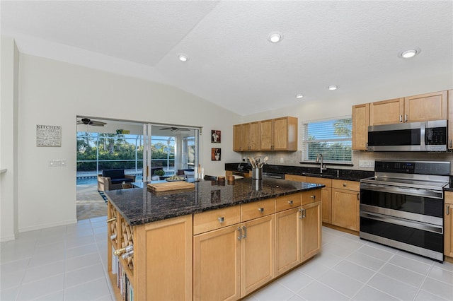 kitchen featuring sink, vaulted ceiling, dark stone countertops, a kitchen island, and stainless steel appliances