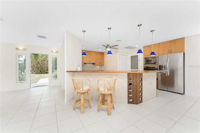 kitchen featuring kitchen peninsula, appliances with stainless steel finishes, decorative backsplash, a kitchen breakfast bar, and light tile patterned floors