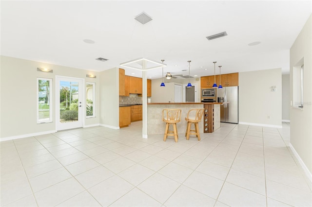 kitchen featuring hanging light fixtures, decorative backsplash, light tile patterned floors, appliances with stainless steel finishes, and a kitchen bar