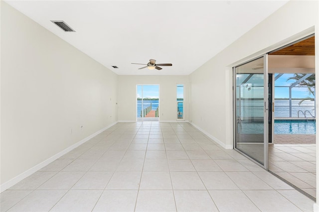 tiled empty room with ceiling fan, plenty of natural light, and a water view