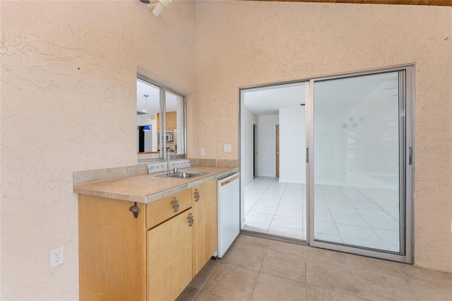 kitchen with light tile patterned floors, light brown cabinets, a sink, light countertops, and dishwasher