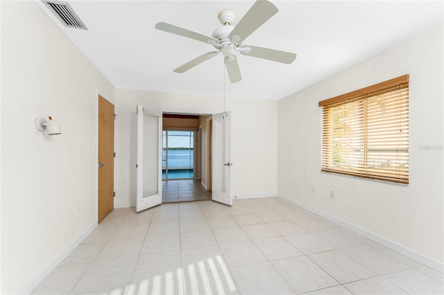 spare room with light tile patterned flooring, visible vents, a ceiling fan, and baseboards