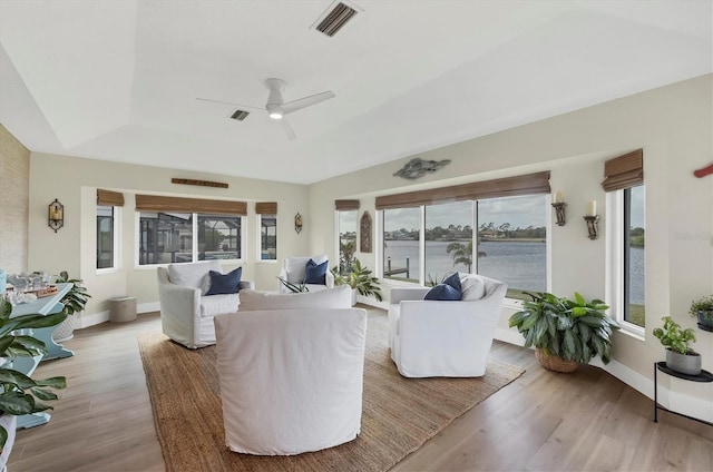 living room featuring ceiling fan, a healthy amount of sunlight, light hardwood / wood-style flooring, a tray ceiling, and a water view