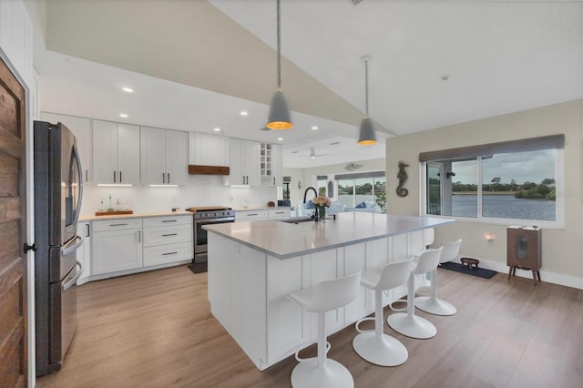 kitchen featuring appliances with stainless steel finishes, a water view, a center island with sink, white cabinetry, and hanging light fixtures