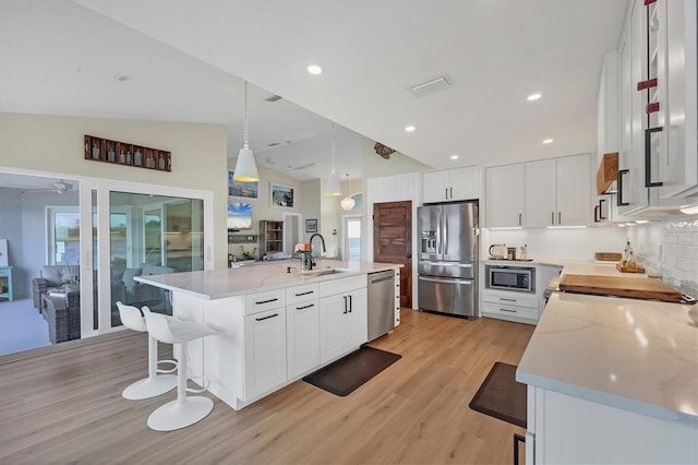 kitchen featuring white cabinetry, sink, stainless steel appliances, decorative light fixtures, and a center island with sink