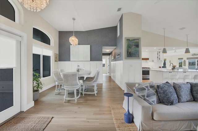 living room with sink, light hardwood / wood-style flooring, high vaulted ceiling, and a notable chandelier