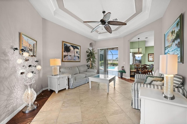 living room featuring a raised ceiling, ceiling fan, and ornamental molding