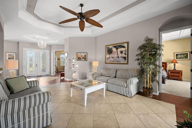 living room with a tray ceiling, french doors, light tile patterned floors, and ceiling fan with notable chandelier