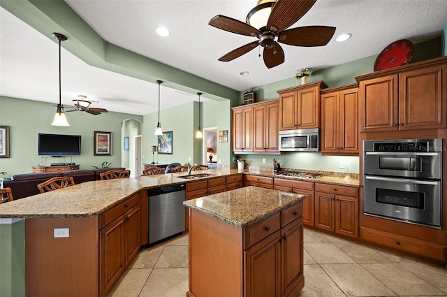 kitchen with kitchen peninsula, appliances with stainless steel finishes, a textured ceiling, pendant lighting, and a center island