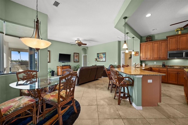 kitchen with pendant lighting, a breakfast bar area, ceiling fan, light stone counters, and stainless steel appliances