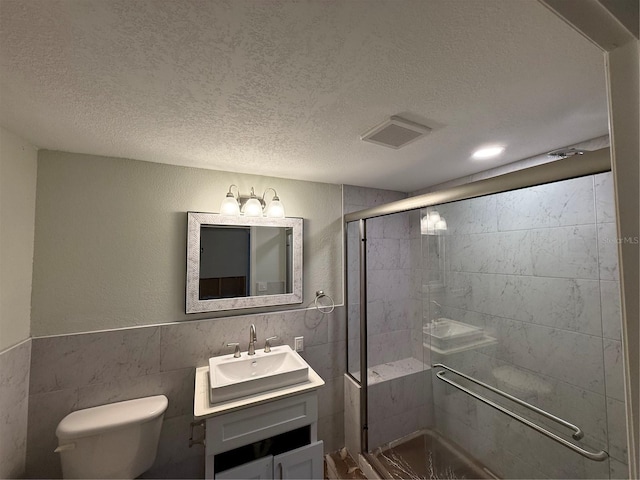 bathroom with vanity, a textured ceiling, a shower with door, and tile walls