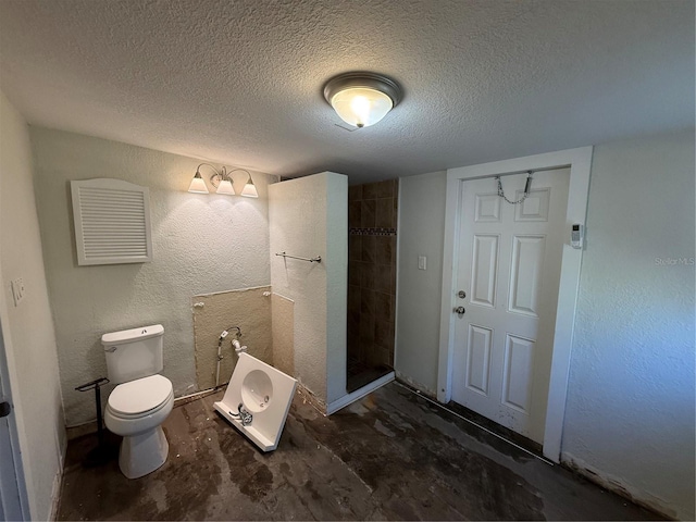 bathroom with toilet, a tile shower, and a textured ceiling