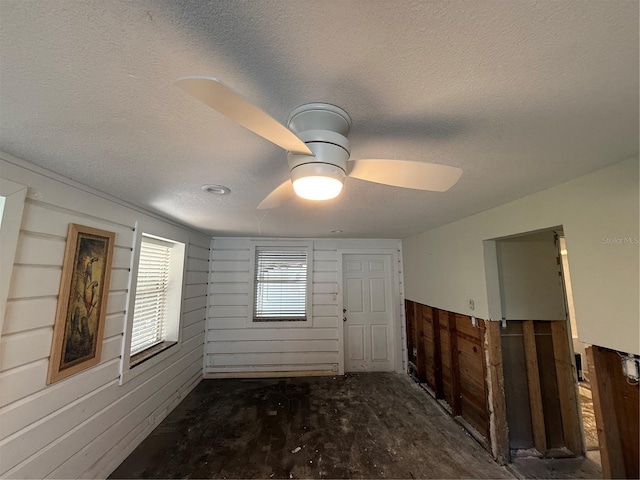 empty room with a textured ceiling, dark wood-type flooring, ceiling fan, and wooden walls