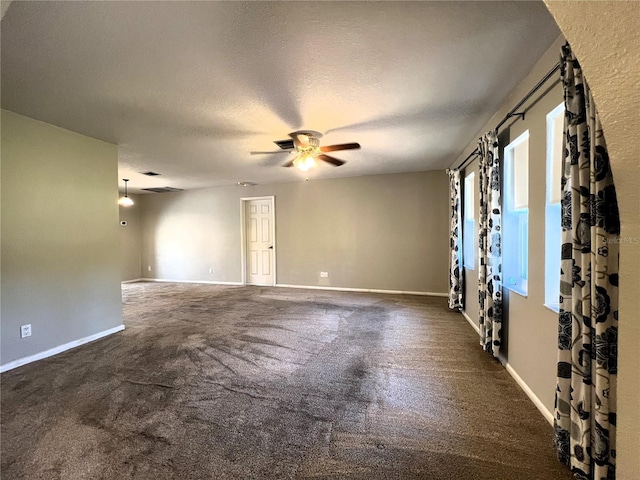 empty room featuring ceiling fan, dark carpet, and a textured ceiling